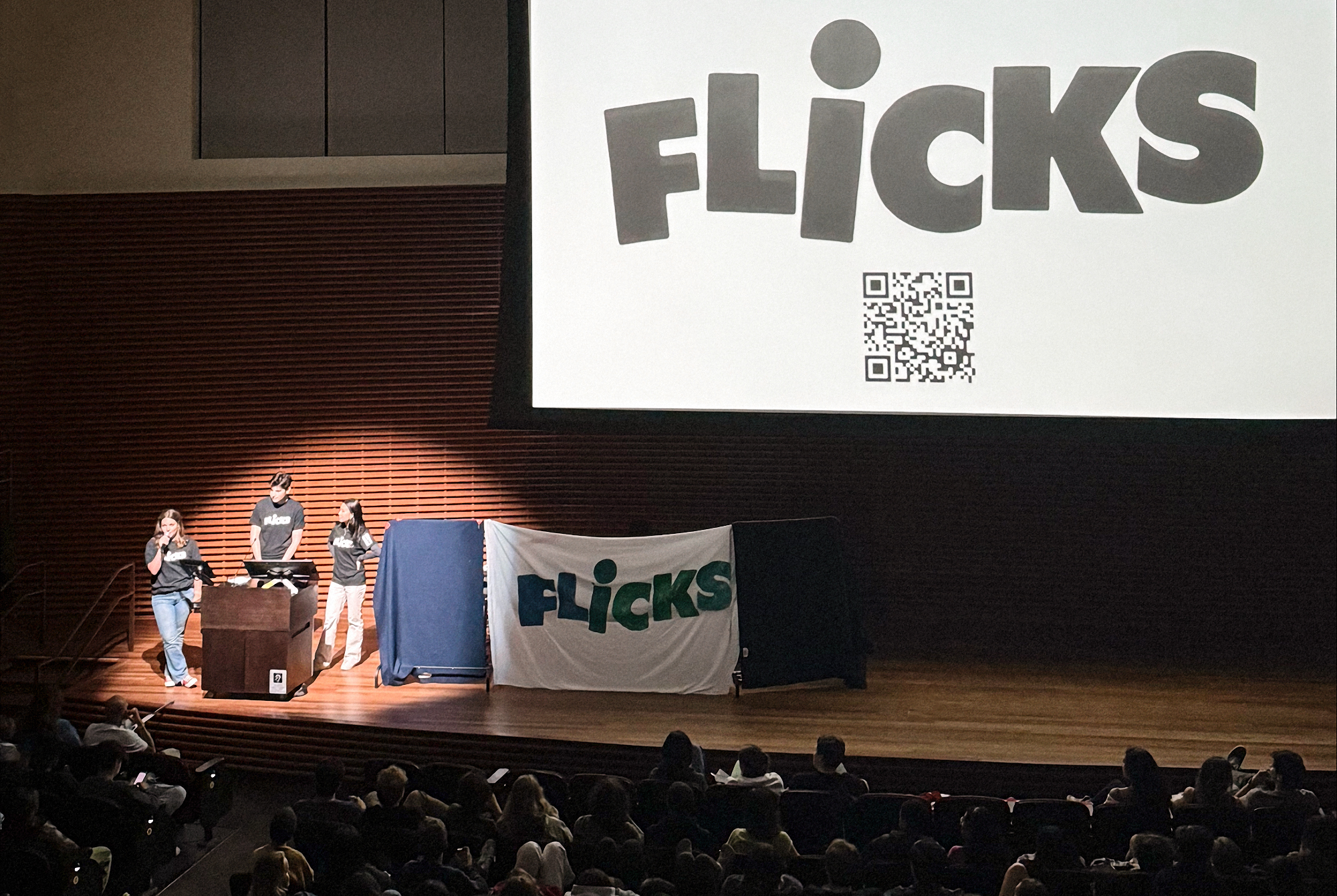 People onstage with a FLiCKS banner 